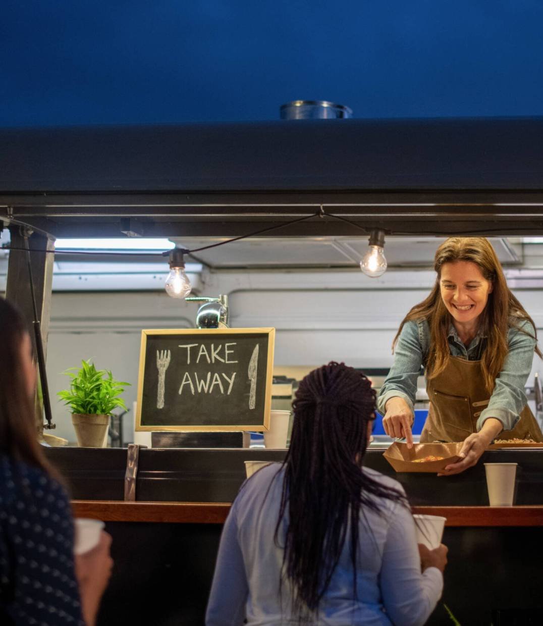 Happy diverse women working in cafe Group of young people in casual clothes sitting at wooden counter in cafe and discussing details of project while working together