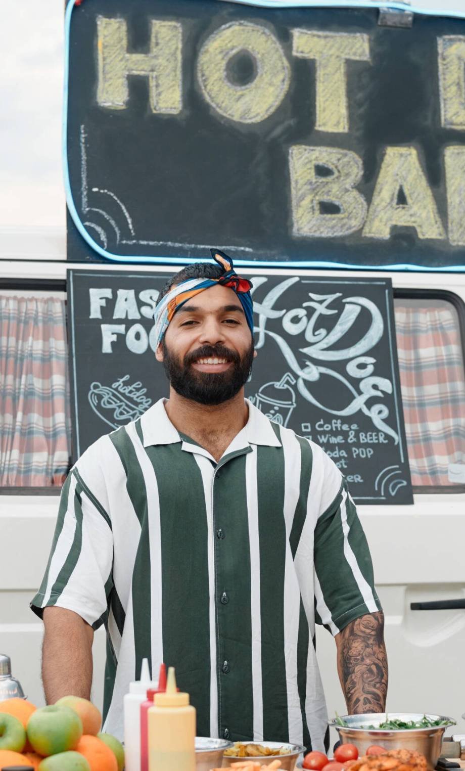 Portrait of young bearded man smiling at camera while selling food outdoors with van in the background